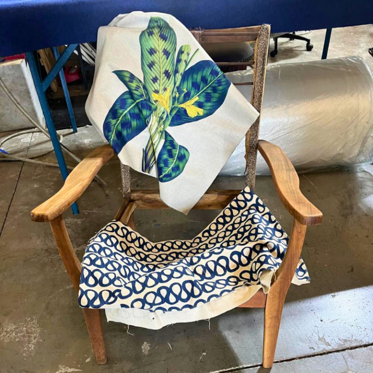 Wooden chair frame with botanical leaf and navy swirl fabric samples during reupholstery.